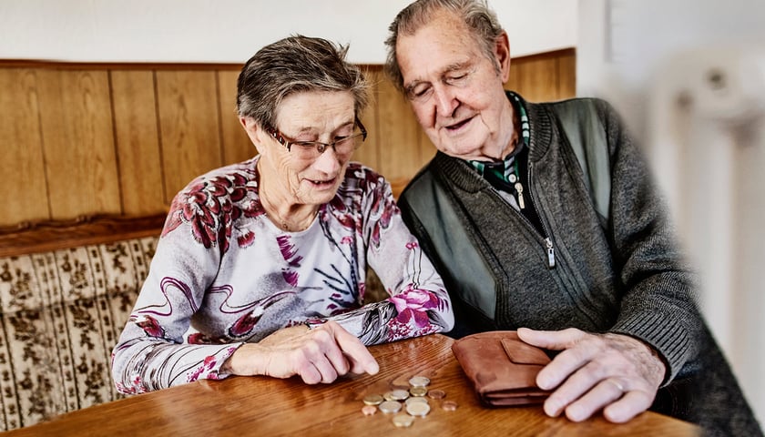 Na zdjęciu starsza kobieta i mężczyzna, na stole lezą monety i portmonetka 
