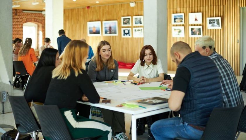 uczestnicy warsztatów o przyszłości Wrocławia podczas spotkania dyskutują siedząc za stołem