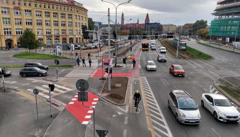 Na zdjęciu dwie trasy dla rowerów, od skrzyżowania ulic - Legnickiej z Rybacką, do przejścia podziemnego pod pl. Jana Pawła II. Po lewej nowa droga rowerowa, po prawej wydzielony pas dla jednośladów na jezdni, po którym jedzie dwóch rowerzystów.