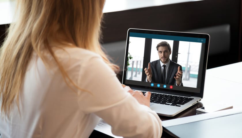 Na zdjęciu widok pleców kobiety, która przez komputer prowadzi rozmowę biznesową z mężczyzną  