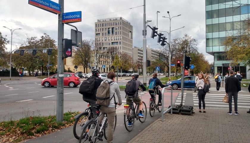 Na zdjęciu skrzyżowanie ulic - Powstańców Śląskich ze Swobodną. Czterech rowerzystów czeka na zmianę światła z czerwonego na zielone.