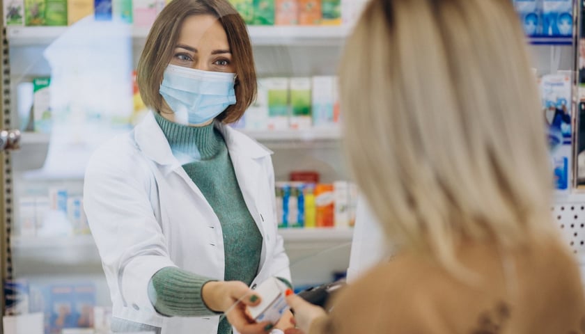 na zdjęciu farmaceutka w maseczce podaje leki odwróconej tyłem kobiecie