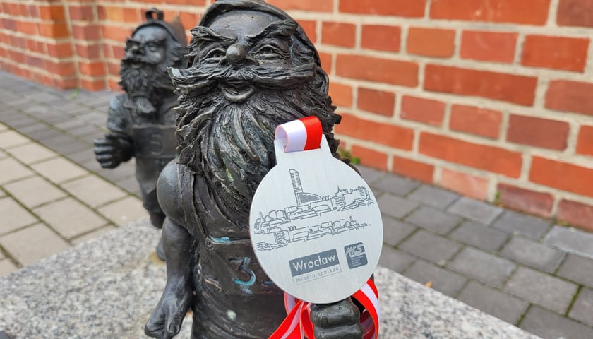 Na zdjęciu dwa krasnale pokazujące  awers medalu - nagrody za ukończenie WrocWalk Marathon 2022