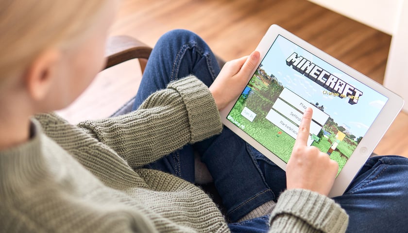 Na zdjęciu nastolatek z tabletem gra w Minecrafta, grę komputerową