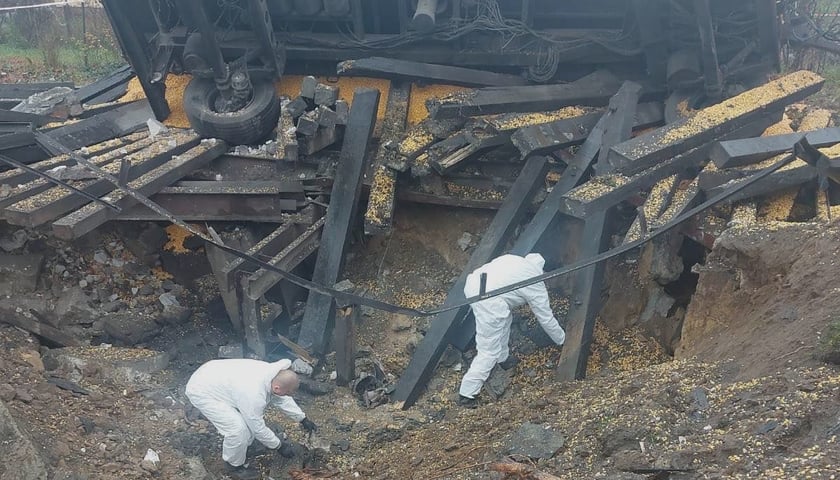 Na zdjęciu krater po wybuchu rakiety w Przewodowie. Dwóch mężczyzn w białych kombinezonach bada miejsce tragedii