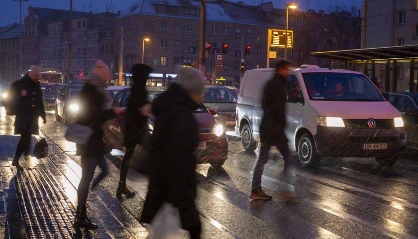 Na zdjęciu piesi na pasach, w tle stojące samochody. Zimowy wieczór, pada marznący deszcz. Zdjęcie ilustracyjne