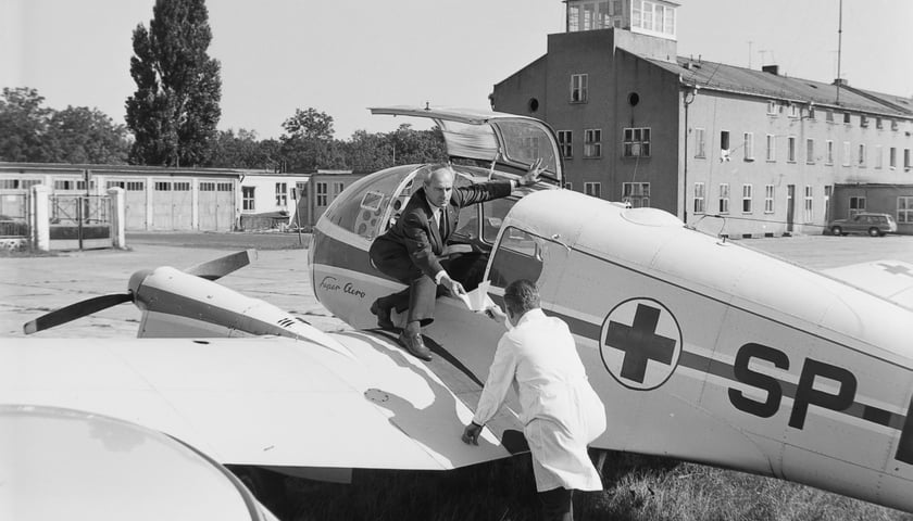 Należący do lotnictwa sanitarnego samolot Aero Ae-45 ?Super Aero? na lotnisku na Gądowie Małym, lata 70. XX w.; z prawej widoczny budynek dworca lotniczego z wieżą kontroli lotów, z lewej ambulans FSO Warszawa (fot. Stanisław Kokurewicz).