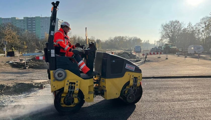 Na zdjęciu robotnik kierujący walcem, którym wyrównuje świeży asfalt na łączniku pomiędzy ulicami - Dembowskiego i Olszewskiego