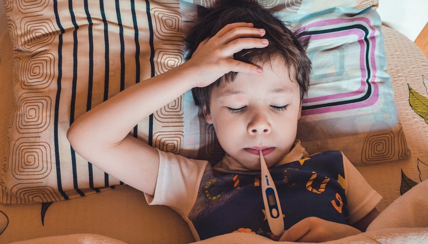 Na zdjęciu chore dziecko, które trzyma termometr w ustach