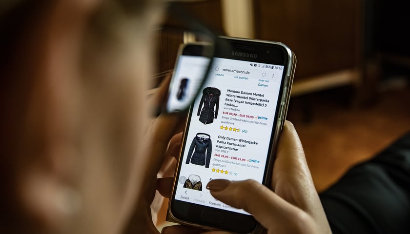Na zdjęciu widać telefon komórkowy, na którym w sklepie internetowym ktoś ogląda ubrania na sprzedaż/zdjęcie ilustracyjne