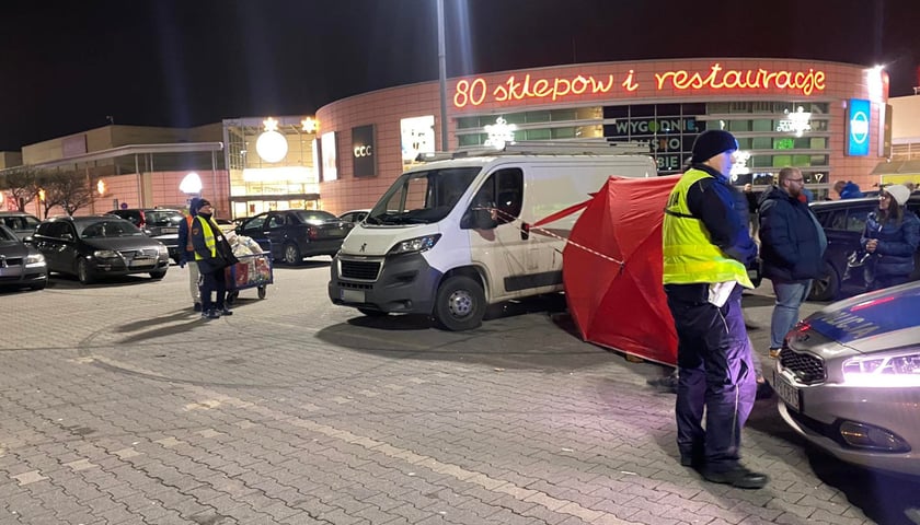 Na zdjęciu radiowóz policyjny, czerwony namiot i miejsce zdarzenia na parkingu Auchan Bielany