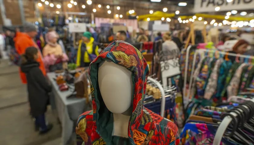 Na zdjęciu manekin ubrany w kolorową bluzę z kapturem. W tle stoiska z odzieżą, osoby oraz osoby odwiedzające targi mody w Czasoprzestrzeni przy ulicy Tramwajowej. Zdjęcie ilustracyjne