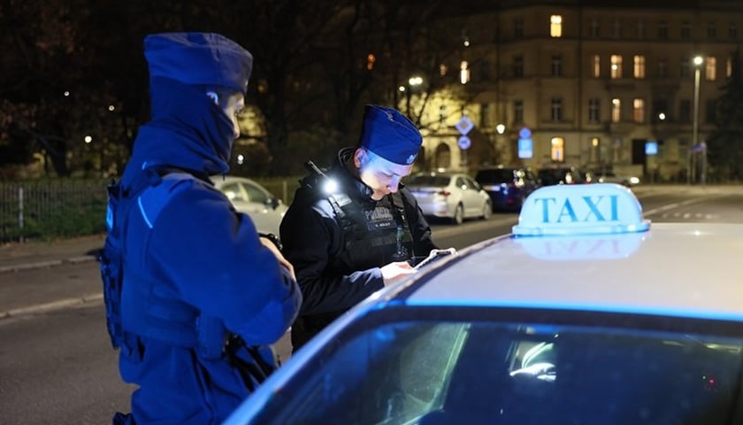 Na zdjęciu dwaj policjanci podczas kontroli dokumentów kierowcy taksówki