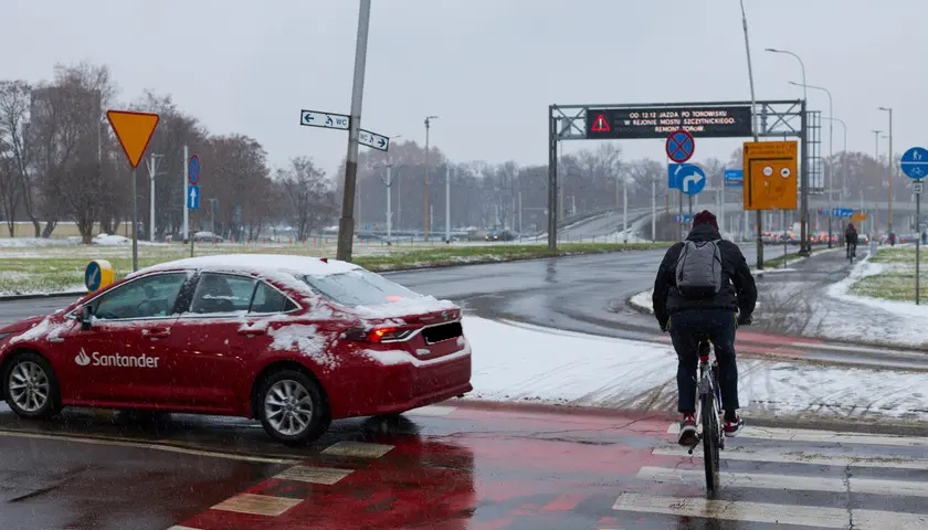 Na zdjęciu ulica zimą; rowerzysta przejeżdża przez jezdnię    