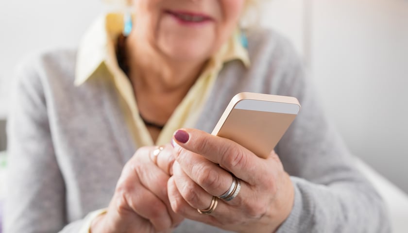 Na zdjęciu starsza pani trzymająca w rękach smartfon.