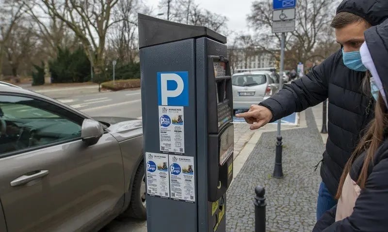 Na zdjęciu dwie osoby stojące przy parkomacie w strefie parkowania