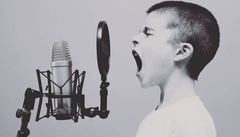 Na zdjęciu chłopiec przed mikrofonem. Mimika dziecka sugeruje krzyk lub śpiew. Zdjęcie ilustracyjne