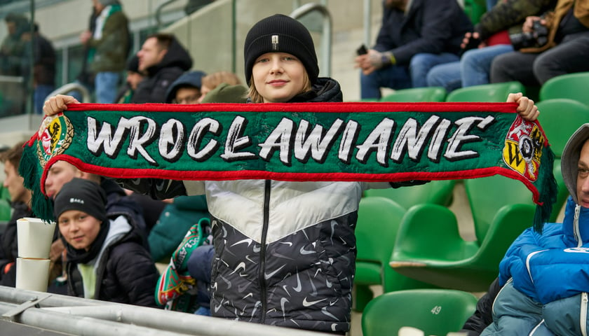 Na zdjęciu widać kibica na stadionie Tarczyński Arena na wrocławskich Pilczycach. W rękach trzyma szalik z napisem "Wrocławianie" 