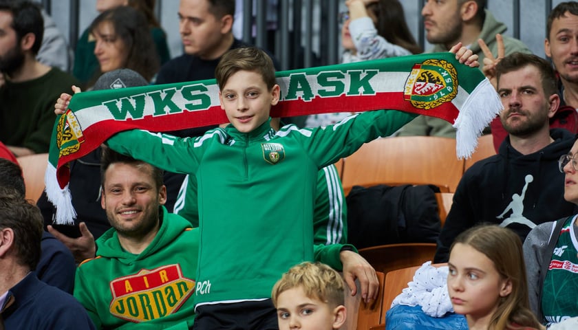 Na zdjęciu: chłopak w zielonej bluzie trzymający szalik nad głową, a także inni kibice Śląska Wrocław