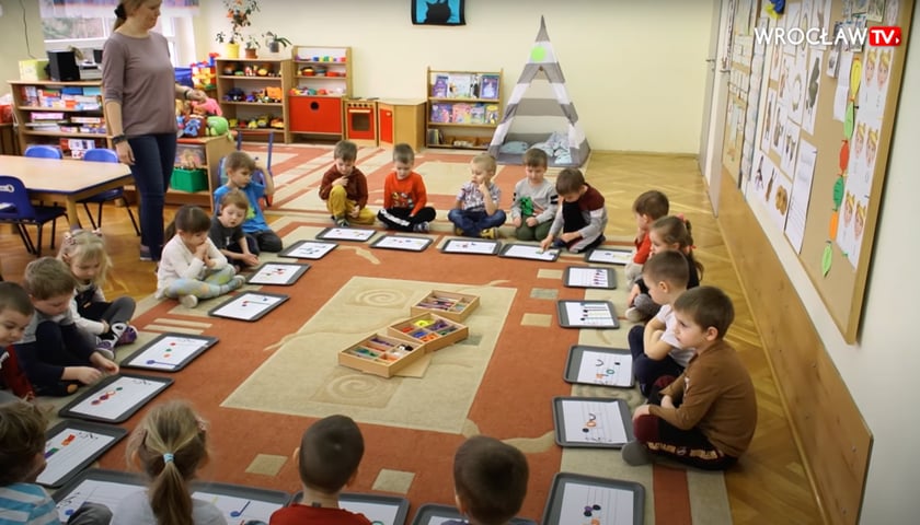 Dzieci z Przedszkola 149 Tęczowa Polanka przy ul. Obornickiej siedzą na dywanie nad ramkami z białymi kartkami