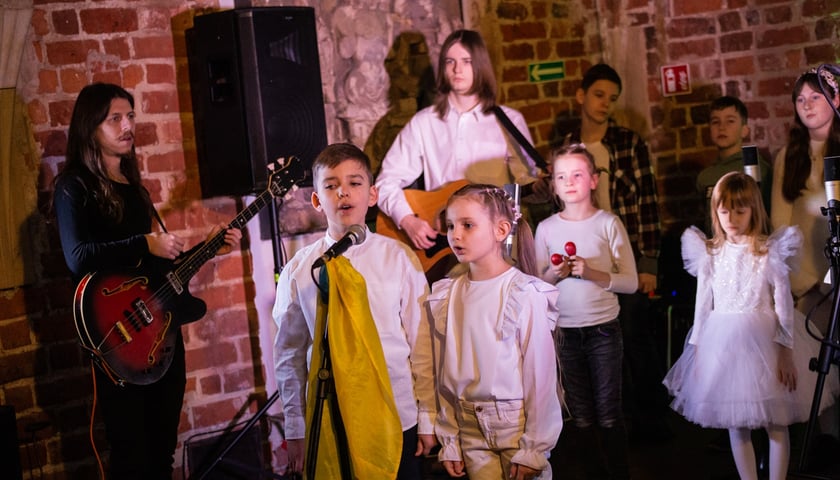 Na zdjęciu koncert zespołu KapustaBand w Muzeum Architektury we Wrocławiu. Na zdjęciu widać chłopca i dziewczynkę stojących i śpiewających przed mikrofonem