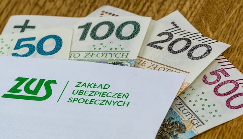 Na zdjęciu widać banknoty i kopertę z napisem ZUS