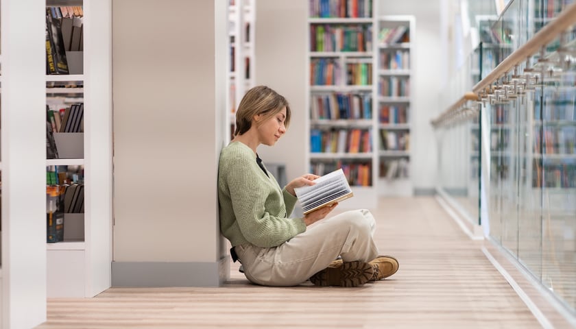 Światowy Dzień Książki, na zdjęciu kobieta czytająca książkę w bibliotece. 