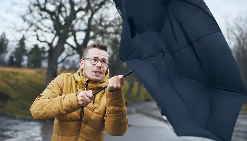 Na zdjęciu mężczyzna z parasolem wygiętym przez wiatr, zdjęcie ilustracyjne
