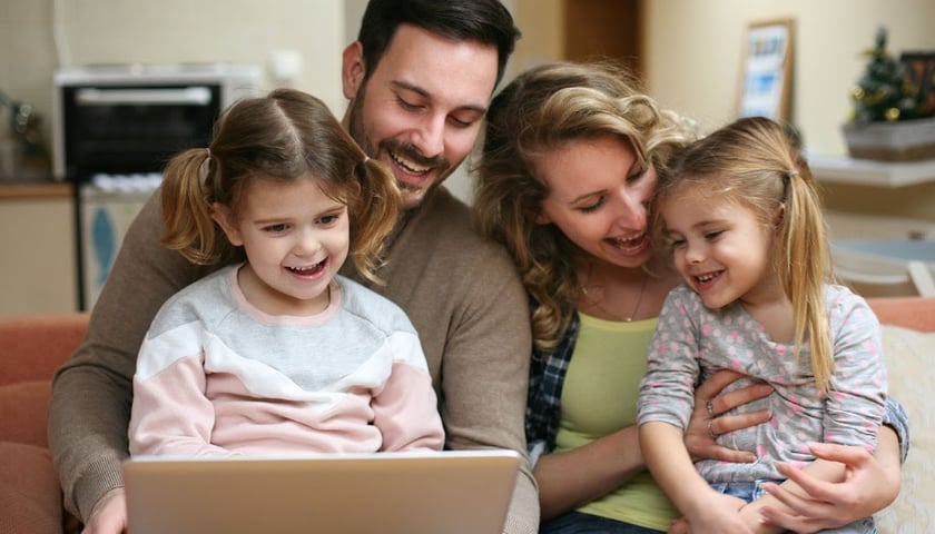 Na zdjęciu widać kobietę, mężczyznę i dwójkę dzieci patrzących na laptopa