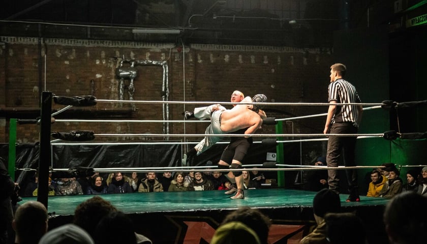 Na zdjęciu dwóch zawodników walczących w ringu podczas zawodów Maniac Zone Wrestling w zajezdni Dąbie. W narożniku ringu stoi sędzia. Wrocław 11.03.2023