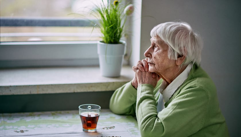 Na zdjęciu seniorka - pani Basia, siedząca samotnie przy stoliku, zapatrzona w okno