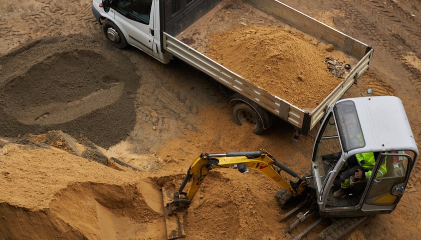 Inwestycja budowlana - minikoparka ładuje piasek na samochód ciężarowy. Zdjęcie ilustracyjne