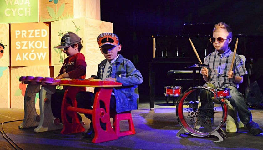Trzech przedszkolaków na scenie. Chłopiec z prawej strony gra na miniaturowej perkusji, dwaj chłopcy z lewej na kolorowych keyboardach. Zdjęcie ilustracyjne z jednej z poprzednich Edycji Festiwalu Śpiewających Przedszkolaków.