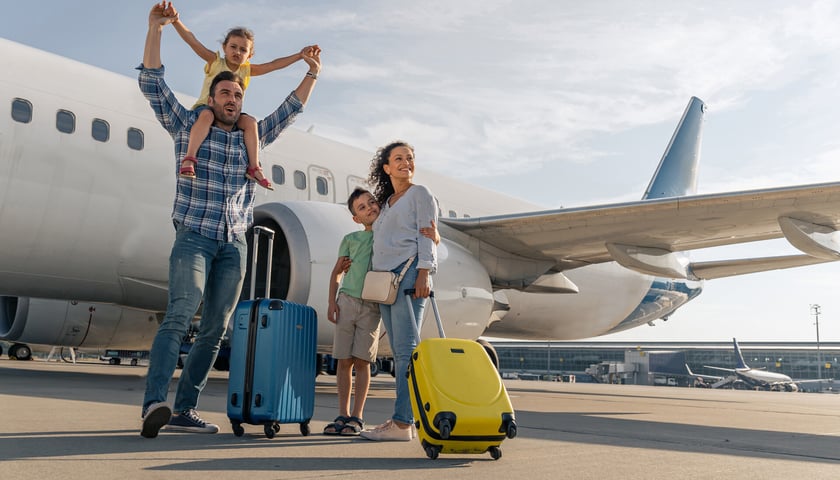 Rodzice z dziećmi na lotnisku, przed podróżą. W tle samolot i terminal lotniska