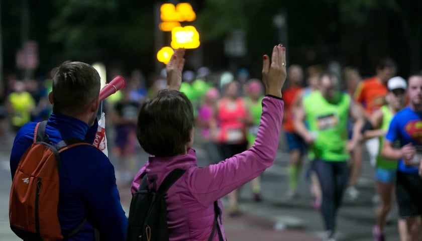 Mężczyzna dmuchający w trąbkę i kobieta unosząca ręce do góry przy trasie półmaratonu we Wrocławiu