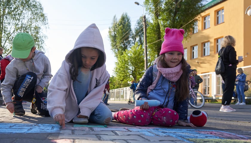 Trójka dzieci koloruje kredami jezdnię 