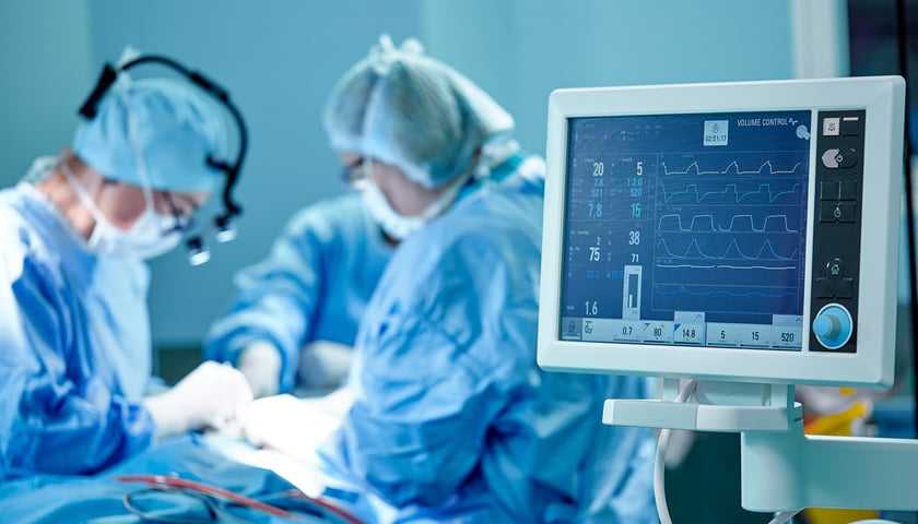 Po lewej sylwetki chirurgów podczas operacji, po prawej monitor z wyświetlonymi funkcjami życiowymi pacjenta  (zdjęcie ilustracyjne)