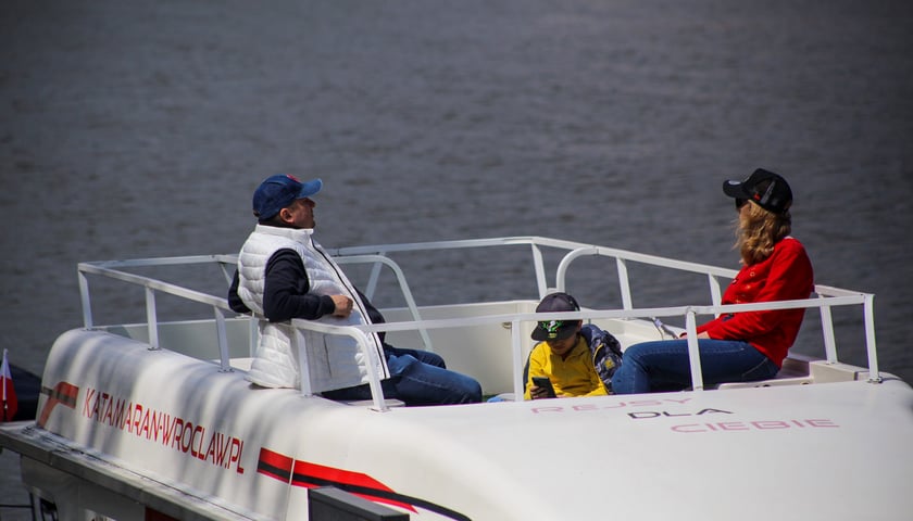 Dni Odry 2023, na zdjęciu trzyosobowa rodzina na pokładzie białego katamaranu, w tle rzeka.