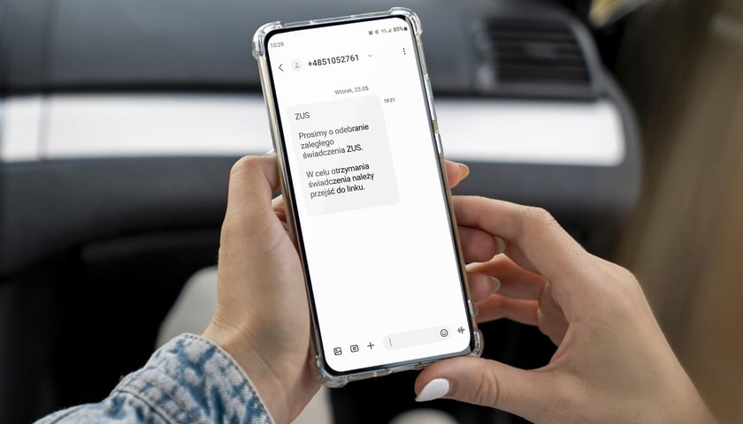 Trzymany w rękach telefon z informacją od internetowych oszustów: wiadomości SMS o odebraniu nieodebranego świadczenia ZUS