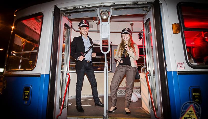 <p>Mężczyzna i kobieta z czapkami konduktorskimi na głowie&nbsp; stoją w wejściui do tramwaju. Zdjęcie zrobione nocą&nbsp;</p>