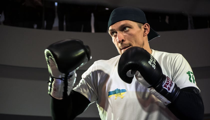 Aleksander Usyk stoi w czapce z daszkiem, w pozycji bokserskiej, w rękawicach