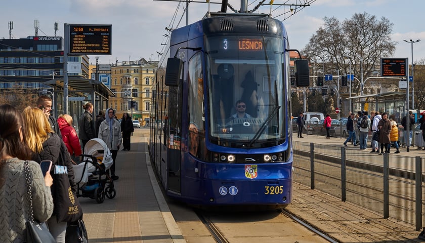 Niebieski tramwaj linii nr 3 na przystanku, na jego przedzie wyświetla się napis "Leśnica". Z lewej strony stoi grupa pasażerów