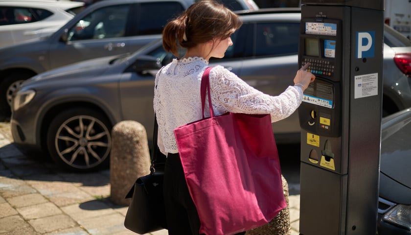 Kobieta z dużą czerwoną torbą stoi przed parkomatem, kupuje bilet 