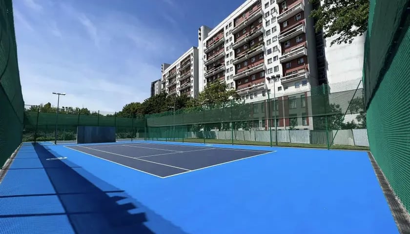 Nowy kort tenisowy przy ul. Trwałej, o nawierzchni w odcieniach błękitu, z prawej bloki 