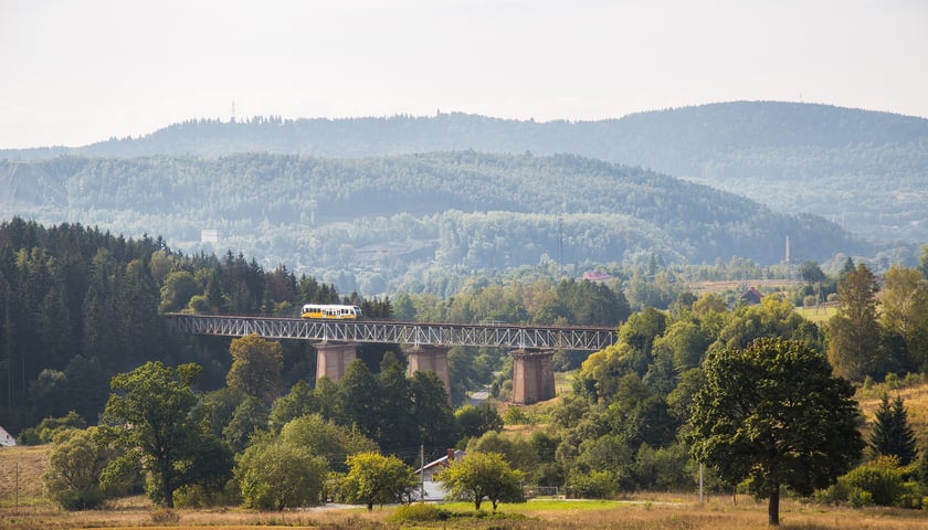 Pociąg KD przejeżdżający mostem kolejowym na tle dolnośląskich gór porośniętych zielenią