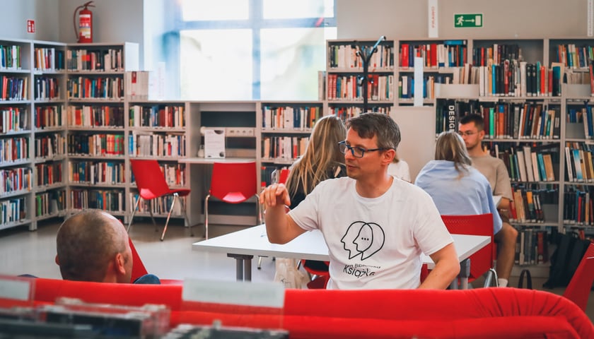 Osoba w koszulce z napisem Żywa Książka rozmawia z Czytelnikiem w bibliotece