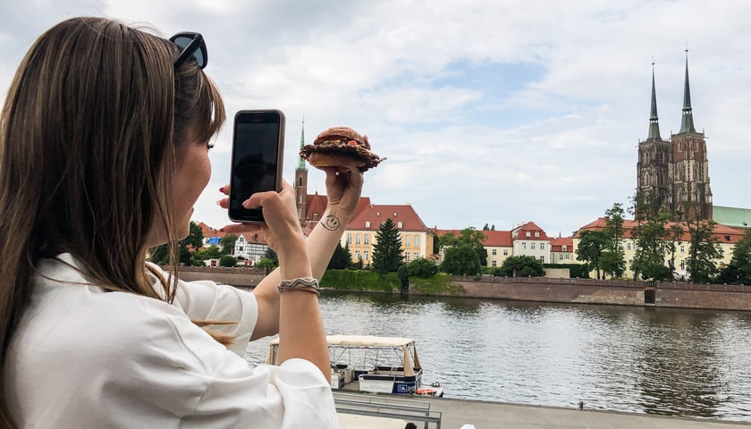 Kobieta na tle Ostrowa Tumskiego fotografuje burgera kupionego podczas Gastro Miasto 