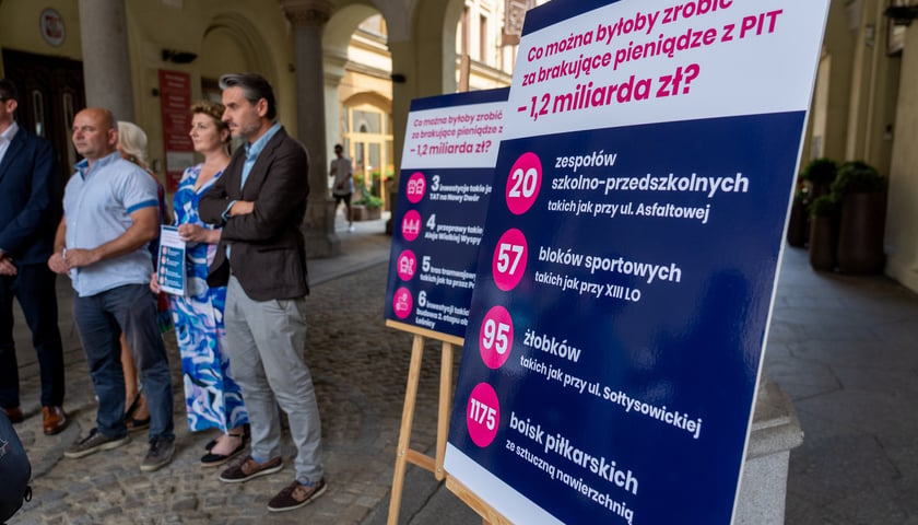 Na zdjęciu tablica, ile we Wrocławiu można zrobić za stracone przez reformę podatkową 1,2 mld złotych, w tle uczestnicy konferencji prasowej
