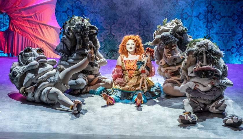 Scena ze spektaklu w Teatrze Lalek, na środku sceny siedzi rudowłosa Ojeja w kolorowej sukience, otaczają ją inni bohaterowie 