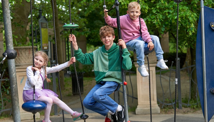 Trójka dzieci w różnym wieku wisi na huśtawkach placu zabaw (zdjęcie ilustracyjne)